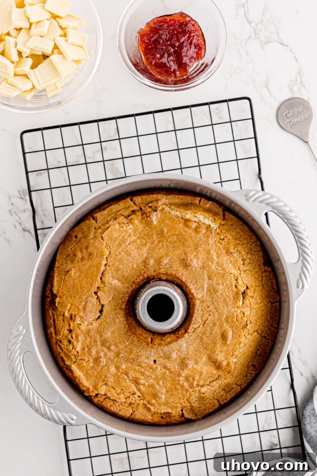 A freshly baked cream cheese pound cake, golden brown and still in its tube pan, cooling gently on a wire rack.