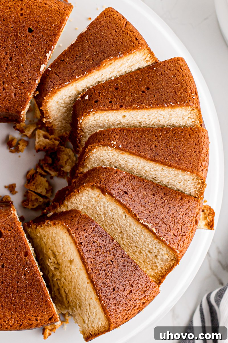 Overhead view of a partially sliced cream cheese pound cake elegantly displayed on a white cake stand, inviting a taste.