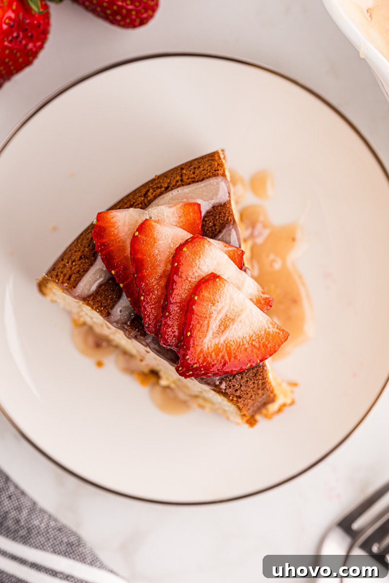 Overhead view of a perfect slice of cream cheese pound cake, generously topped with strawberry white chocolate sauce and garnished with fresh sliced strawberries on a clean white plate.