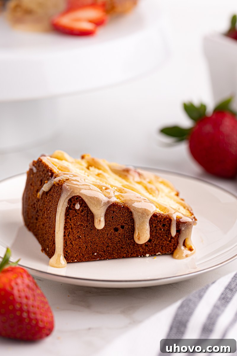 A delectable slice of cream cheese pound cake topped with a generous swirl of strawberry white chocolate sauce, presented on a simple white plate.