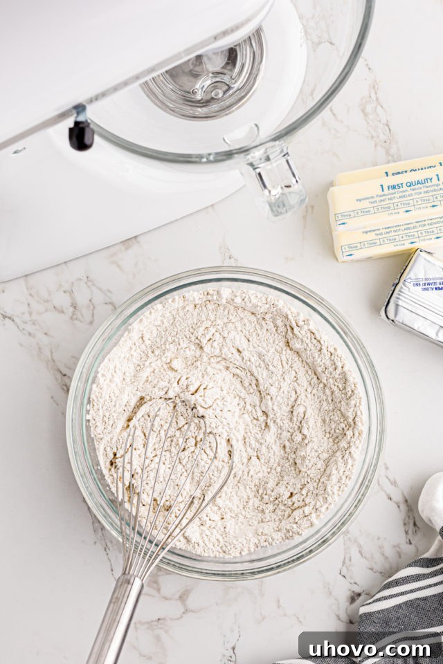 Overhead view of all-purpose flour and salt precisely measured and combined in a clear glass mixing bowl, ready for the next step.