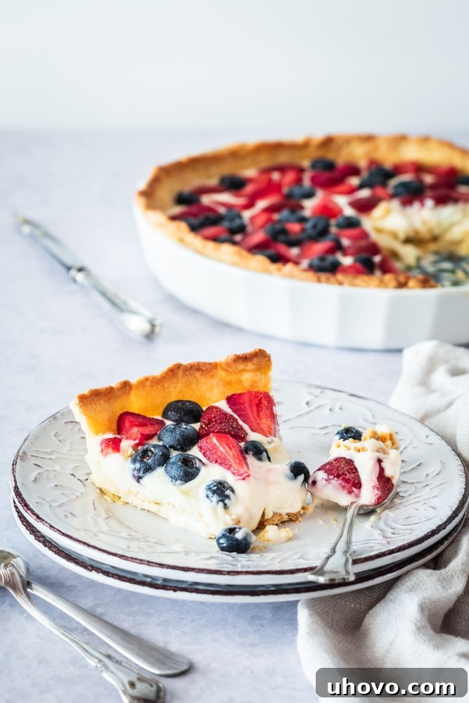 Slice of fresh berry tart on dessert plate with spoon