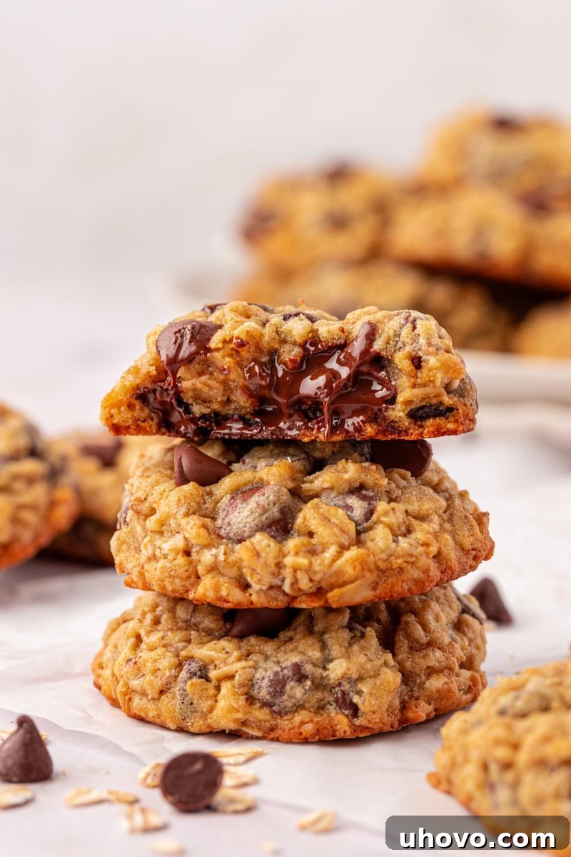 Stack of three soft and chewy brown sugar oatmeal chocolate chip cookies, with a small bite missing from the top cookie, showcasing their delicious texture and chocolatey centers.