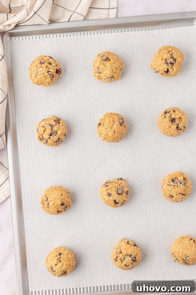 Overhead view of evenly portioned brown sugar oatmeal chocolate chip cookie dough balls on a parchment-lined baking sheet, ready for the oven.