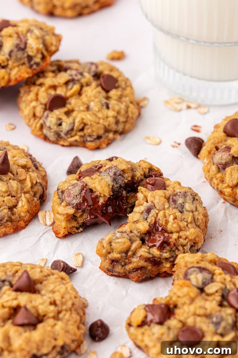 Several brown sugar oatmeal chocolate chip cookies arranged on a white surface with a glass of milk partially visible in the blurred background, creating a cozy and inviting scene.