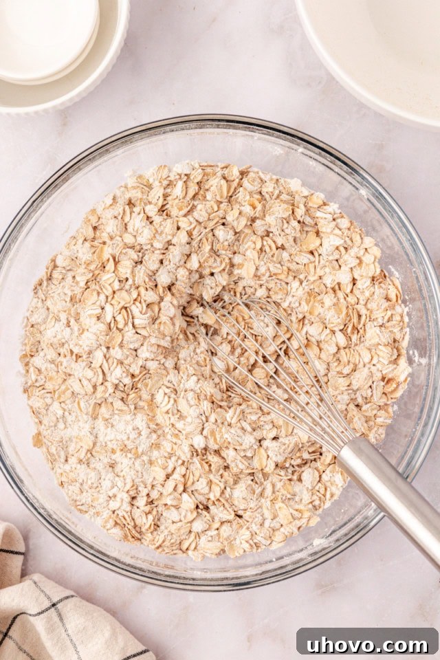 Overhead view of old-fashioned oats being stirred into the dry ingredient mixture for brown sugar oatmeal chocolate chip cookies.