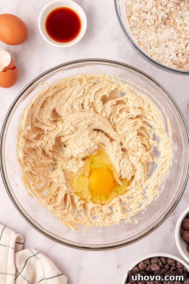 Overhead view of an egg being added to the creamed butter and brown sugar mixture in a mixing bowl.