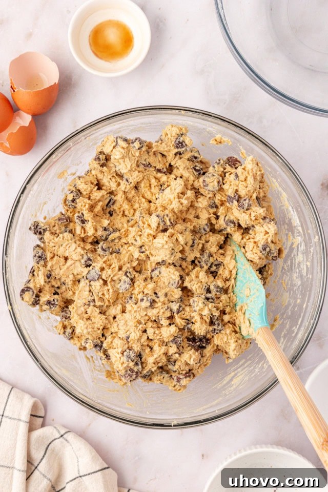 Overhead view of freshly mixed brown sugar oatmeal chocolate chip cookie dough resting in a glass mixing bowl, ready for chilling.