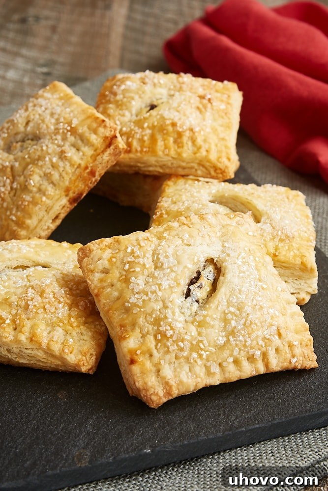 A generous pile of freshly baked Chocolate Chip Cream Cheese Hand Pies, with their golden-brown, flaky crusts visible, resting on a dark serving tray, inviting you to grab one.