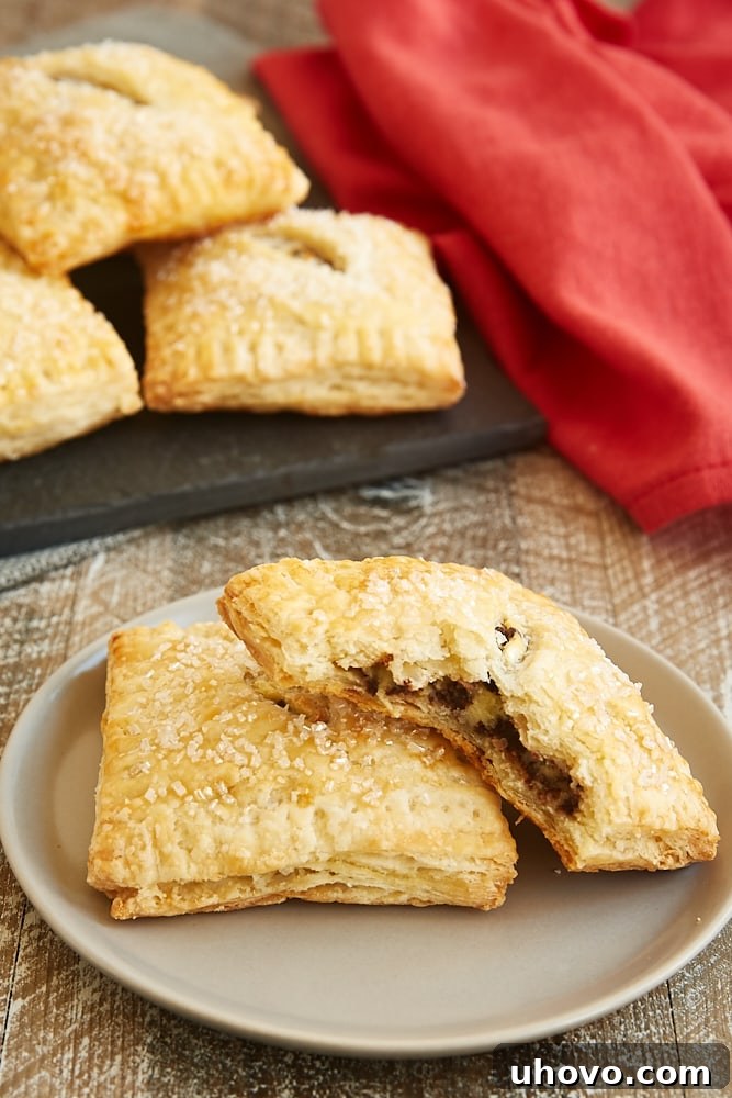 A single, perfectly golden-brown Chocolate Chip Cream Cheese Hand Pie resting on a light gray plate, showcasing its square shape, crimped edges, and a hint of the creamy filling peeking through.