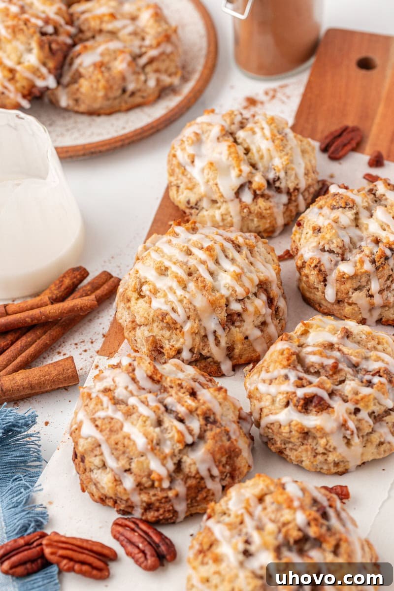 Buttery cinnamon bun scones with a sweet glaze, arranged on a rustic wooden board and a white plate in the background.