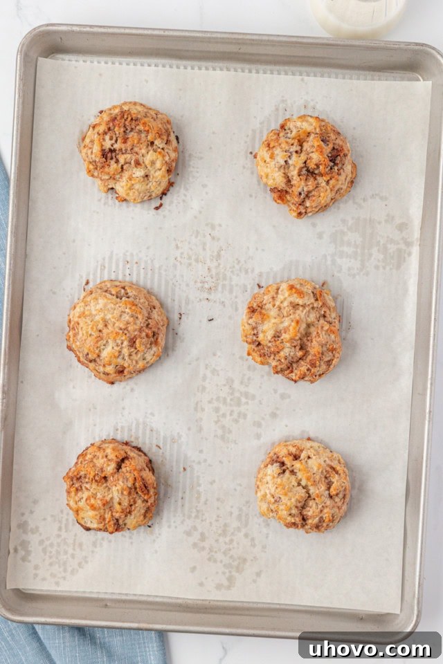 Overhead view of freshly baked, golden-brown cinnamon bun scones cooling slightly on a parchment-lined baking sheet.