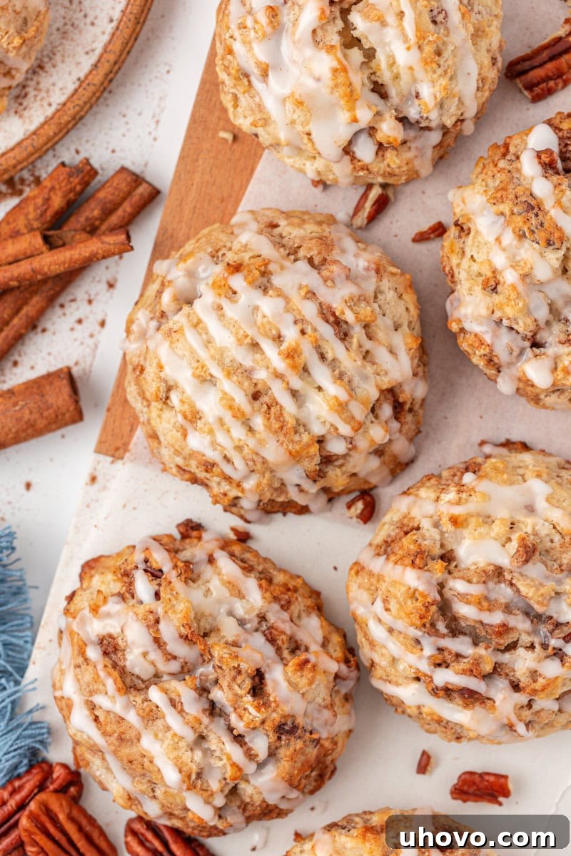 Overhead view of several glazed cinnamon bun scones perfectly arranged on a rustic wooden board, showcasing their inviting texture.