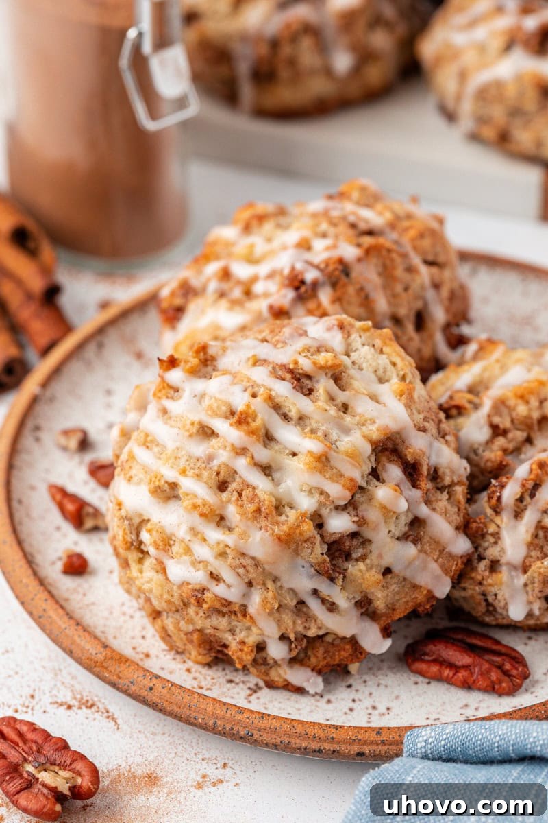 Three perfectly baked and glazed cinnamon bun scones artfully arranged on a white plate, ready to be enjoyed.