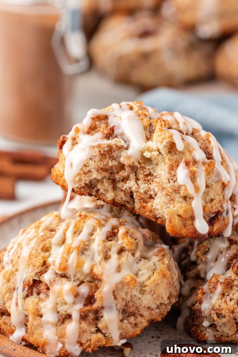 A stack of warm, glazed cinnamon bun scones on a plate, with a bite taken out of the top scone, revealing its tender, swirled interior.