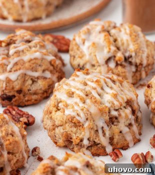 A collection of cinnamon bun scones, some glazed, on a white surface with more scones in the background.