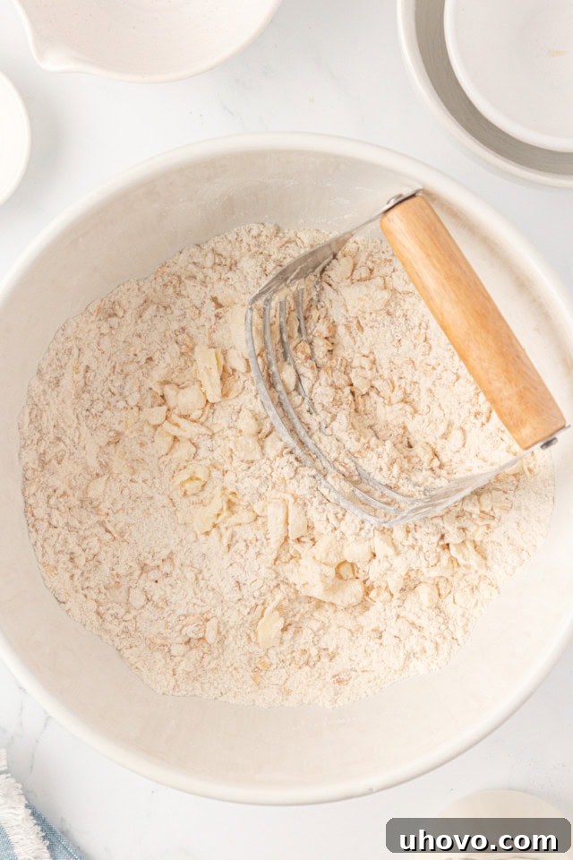 Overhead view of cold butter cubes being cut into the dry flour mixture in a white bowl, resembling coarse crumbs.