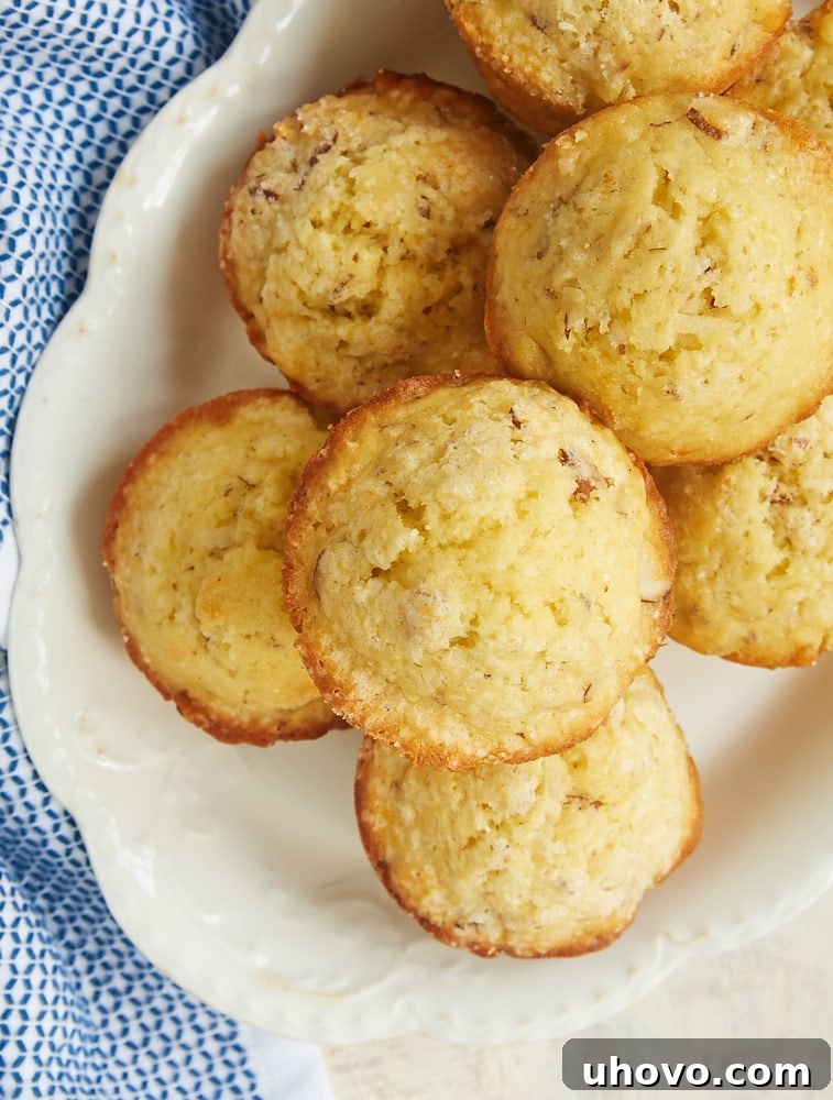 Overhead view of several golden-brown Coconut Almond Muffins on an oval white tray, showcasing their perfectly domed tops and inviting crumb.