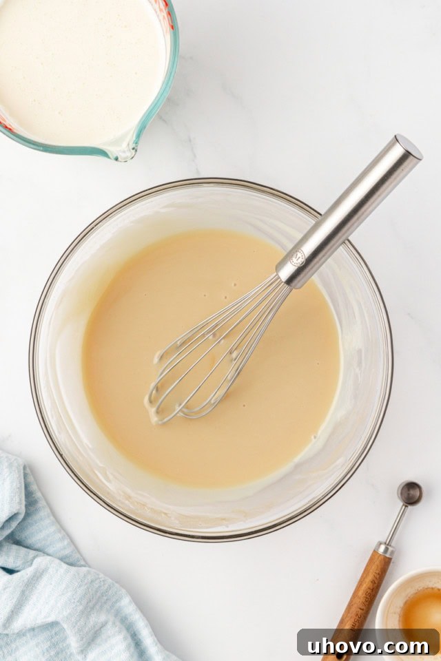 overhead view of condensed milk, vanilla, and salt mixed together in a glass mixing bowl