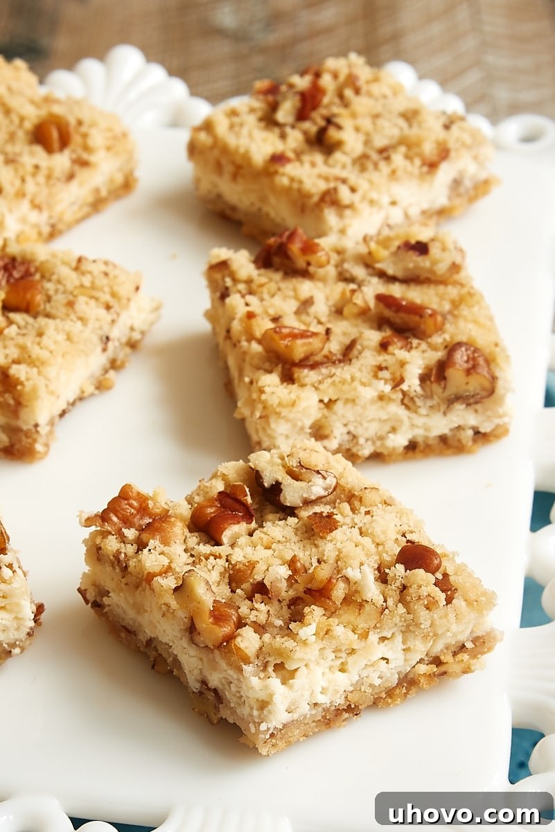 Perfectly sliced Pecan Cheesecake Bars arranged neatly on a pristine white serving tray, showcasing their distinct layers of crumbly crust, creamy filling, and nutty topping.