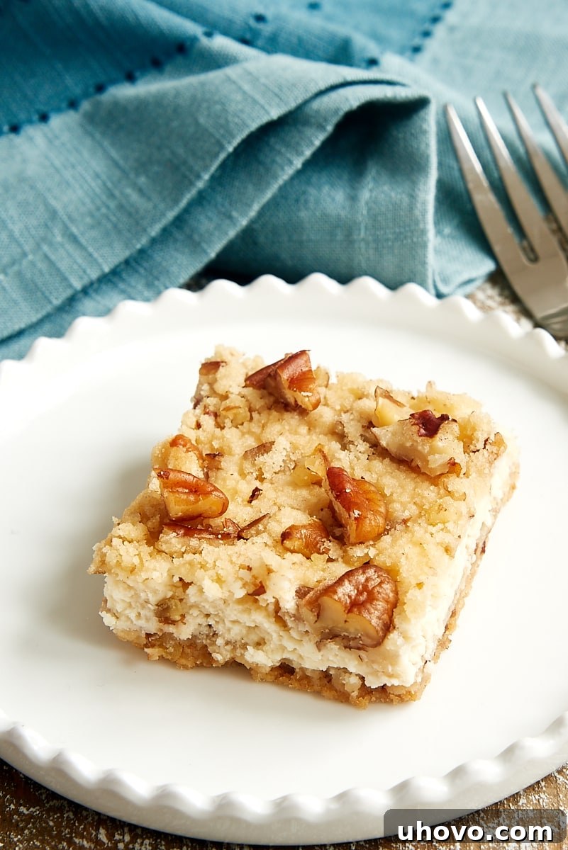 A single, perfectly cut Pecan Cheesecake Bar resting on a small, elegant round white plate, ready to be enjoyed as a personal treat.
