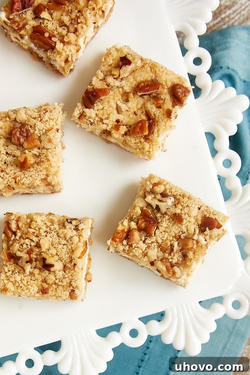 An inviting overhead view of a white platter abundantly filled with perfectly arranged Pecan Cheesecake Bars, each topped with a delicate sprinkle of chopped pecans.