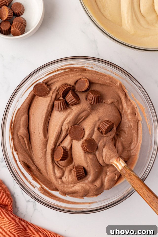 Mini peanut butter cups are being carefully folded into the chocolate ice cream mixture in a glass bowl, after the whipped cream has been incorporated.