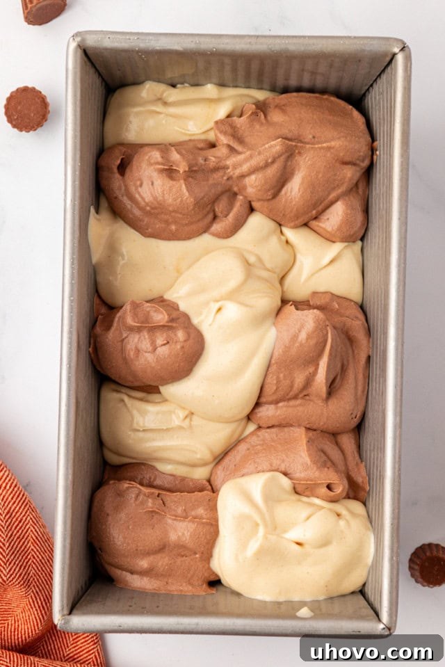 An overhead shot showing scoops of the chocolate and peanut butter ice cream mixtures being alternately placed into a metal loaf pan, creating distinct layers.
