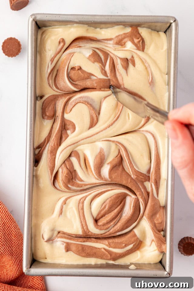 A thin knife is shown swirling through the alternating layers of chocolate and peanut butter ice cream in a metal loaf pan, creating a beautiful marbled effect before freezing.