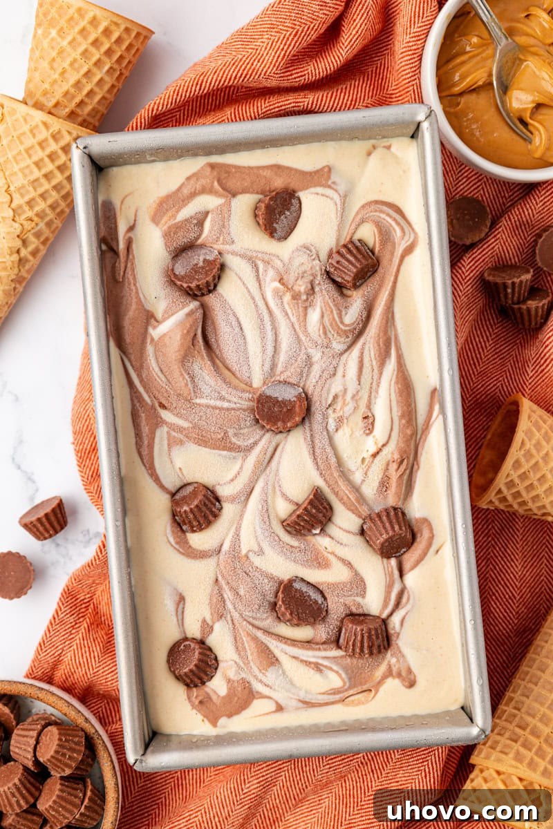 An inviting overhead view of a metal loaf pan filled with perfectly set no-churn chocolate peanut butter swirl ice cream, glistening and ready to be scooped after hours in the freezer.