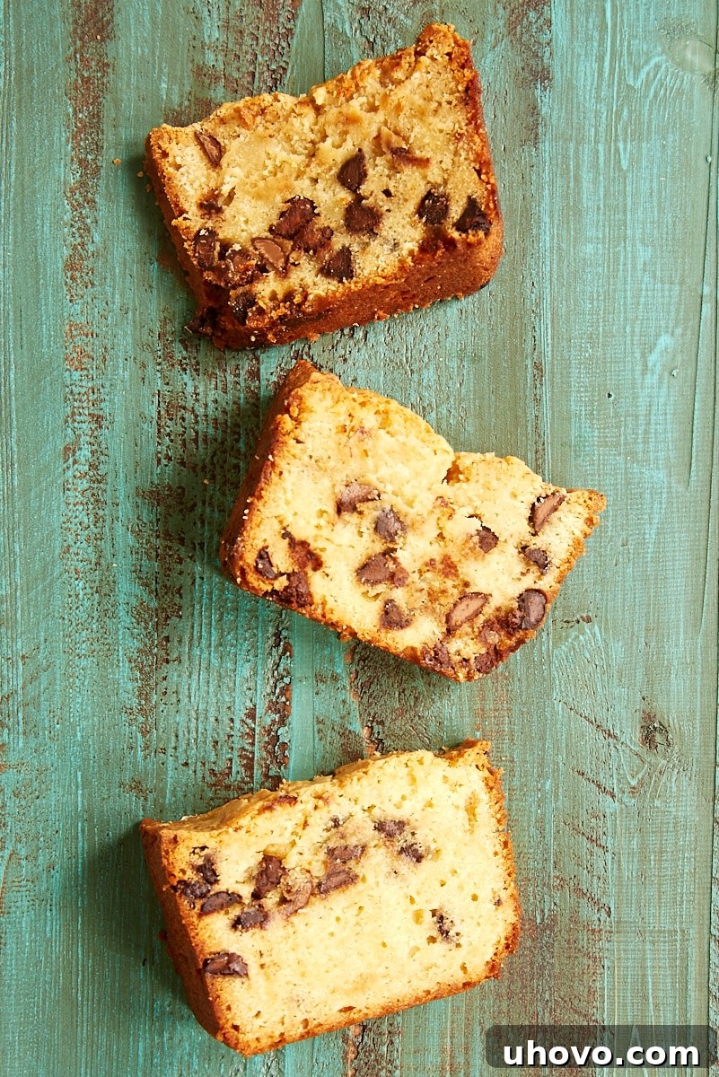 An inviting overhead shot of three perfectly cut slices of Chocolate Chip Cream Cheese Pound Cake artfully arranged on a rustic green wooden surface, highlighting the cake's perfect texture and even chocolate chip distribution.