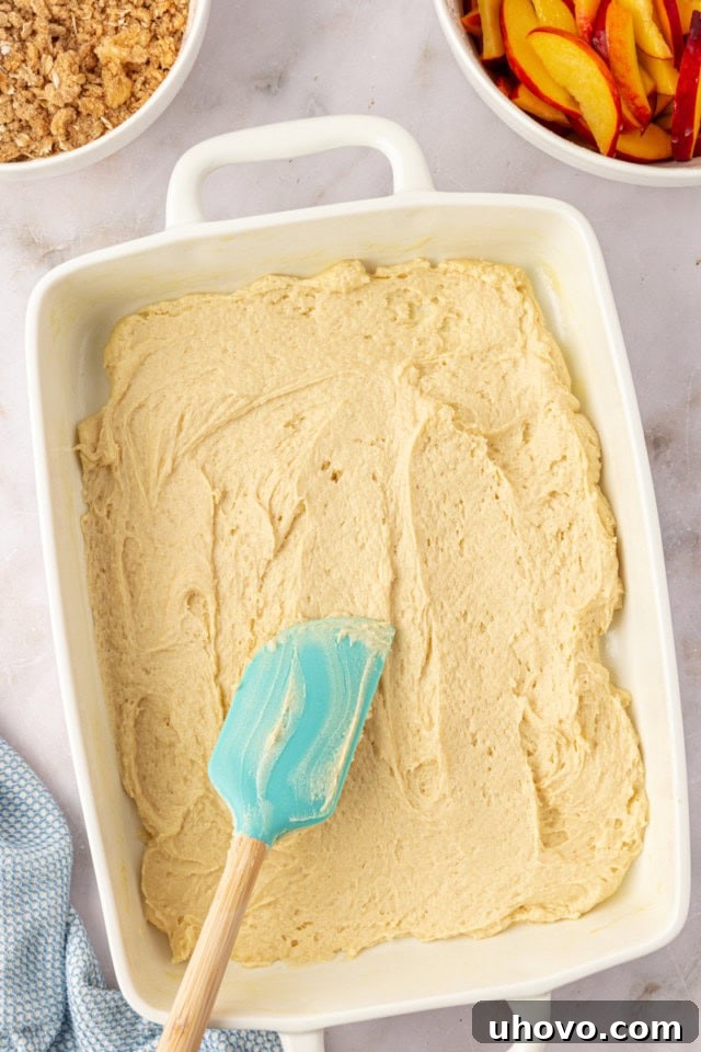 An overhead view of a thick, creamy peach coffee cake batter perfectly spread across the bottom of a rectangular baking pan, forming the first foundational layer.