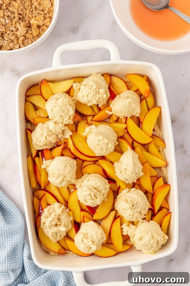 An overhead view showing the remaining cake batter gently dolloped over the peach layer in the baking pan, preparing to be spread evenly to create a harmonious two-layer cake.