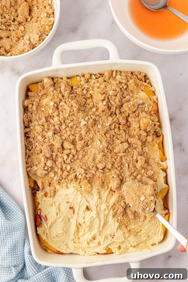 An overhead shot capturing the moment the golden, buttery crumb topping is generously sprinkled over the peach coffee cake batter, promising a delightful crunch with every bite.
