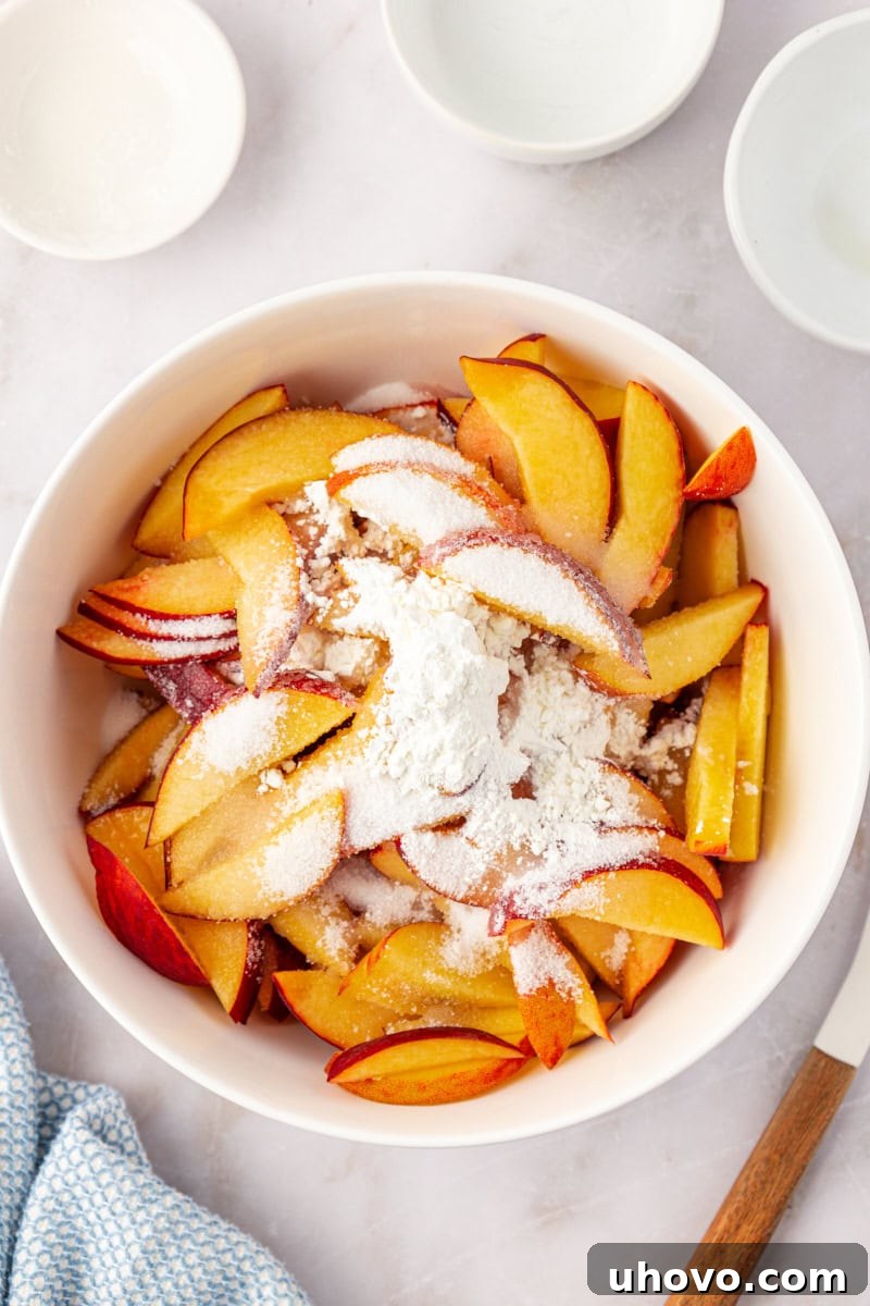 An overhead view of sliced peaches, granulated sugar, fresh lemon juice, and cornstarch expertly combined in a white mixing bowl, ready to become the delicious filling for the coffee cake.