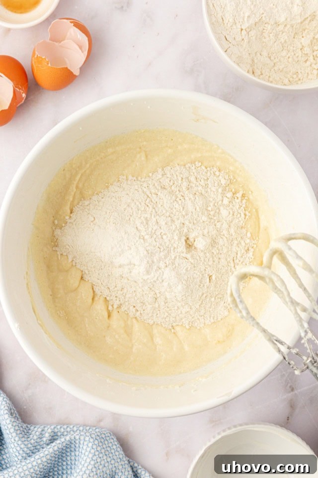 An overhead view illustrating the gradual addition of dry ingredients to the wet mixture for the peach coffee cake, ensuring careful combination without overmixing.