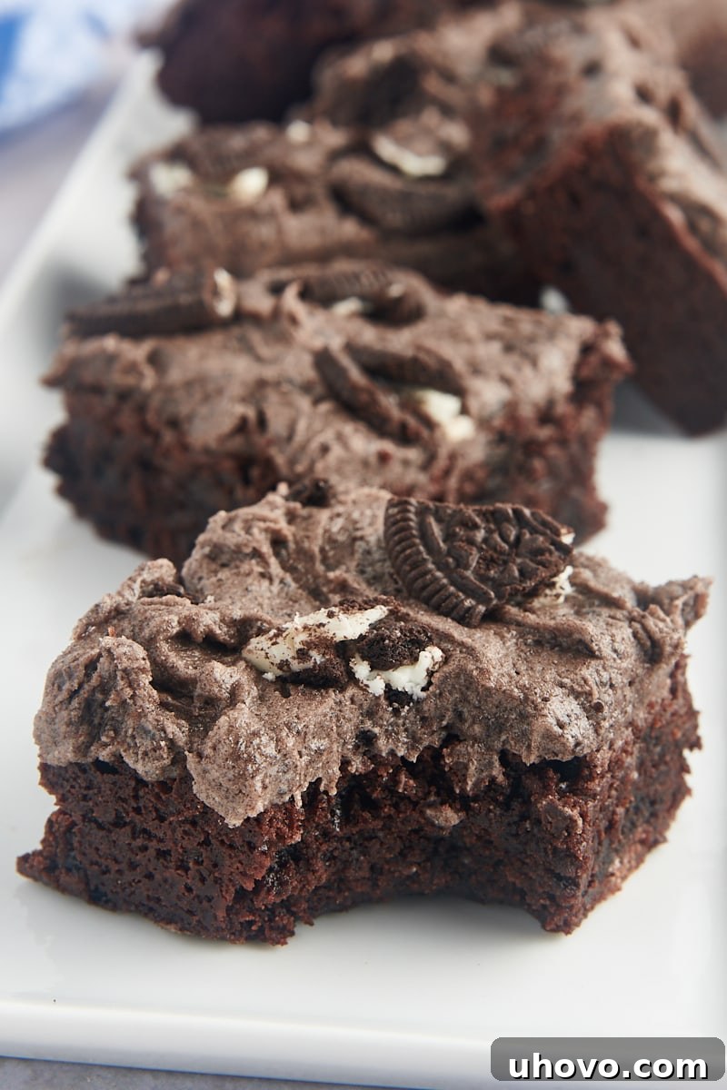 Decadent Oreo brownies arranged on a tray, with one brownie having a bite taken out, revealing its rich, fudgy interior and crunchy cookie pieces.