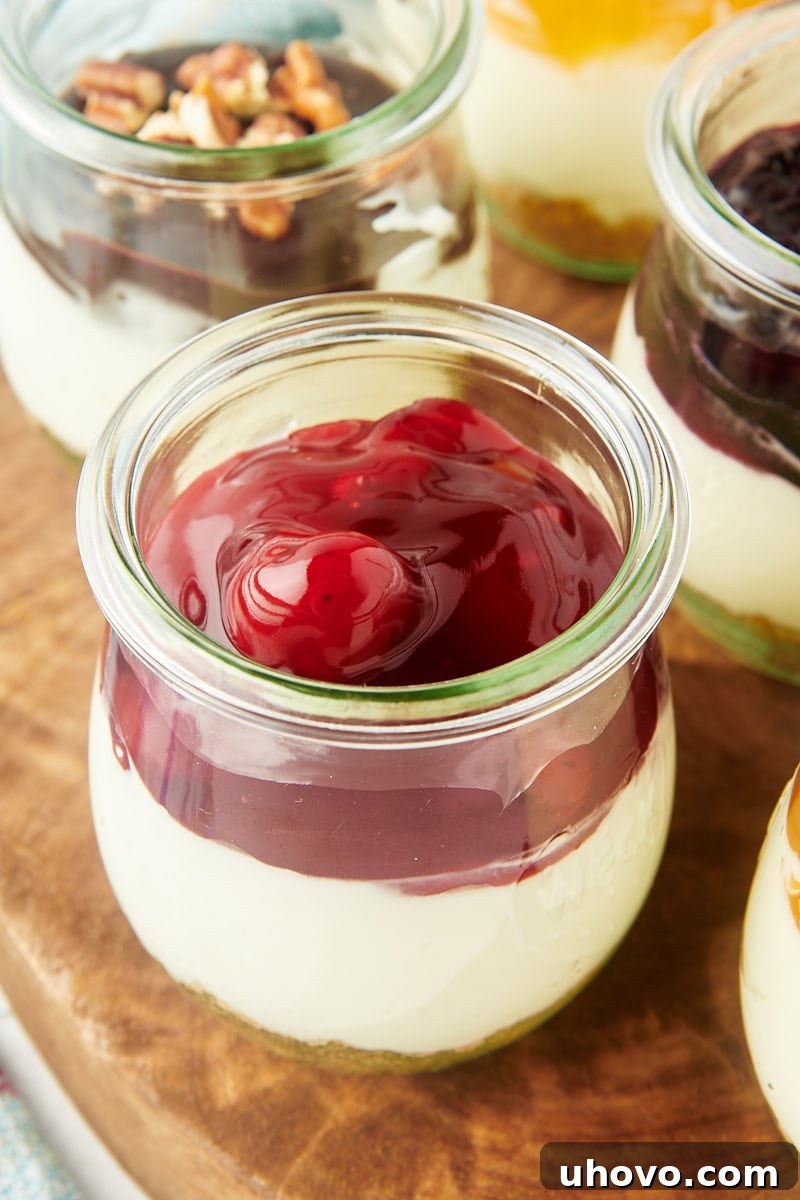 Close-up view of a delightful no-bake cheesecake jar, beautifully layered and generously topped with vibrant cherry pie filling, ready for individual enjoyment.