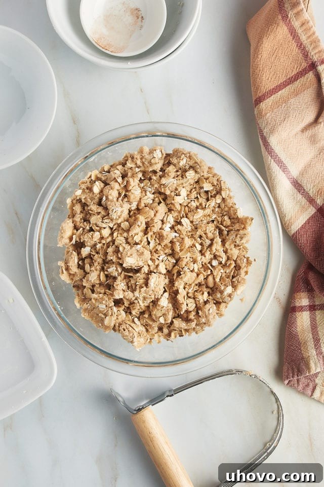 A glass mixing bowl filled with the completed apple crumb topping, a mixture of flour, brown sugar, cinnamon, butter, and oats, ready to be sprinkled over the pie filling.