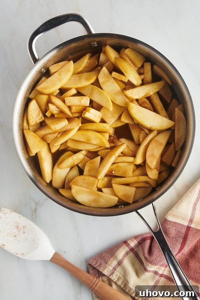 Overhead view of the apple crumb pie filling simmering in a large saucepan on the stovetop, with a rich, thickened, caramel-like sauce coating the apple slices.