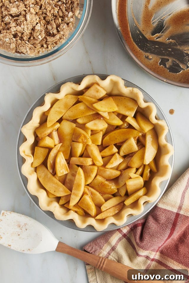 Overhead shot of the cooked apple pie filling being carefully poured into the unbaked pie crust, which is nestled in a pie plate.