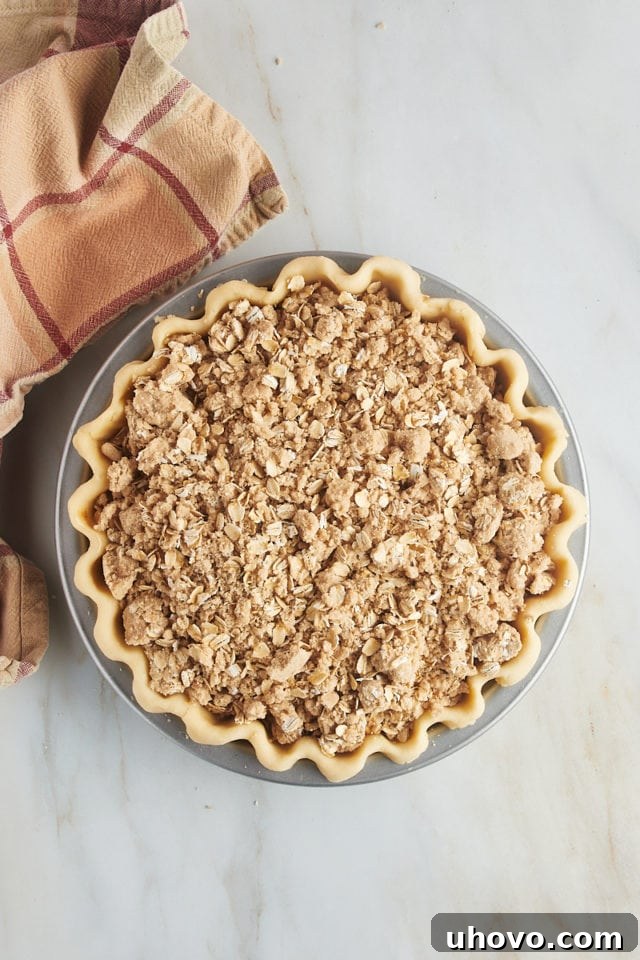 Overhead view of an assembled apple crumb pie, topped with a generous layer of streusel, sitting in its pie plate and ready to be placed in the oven.