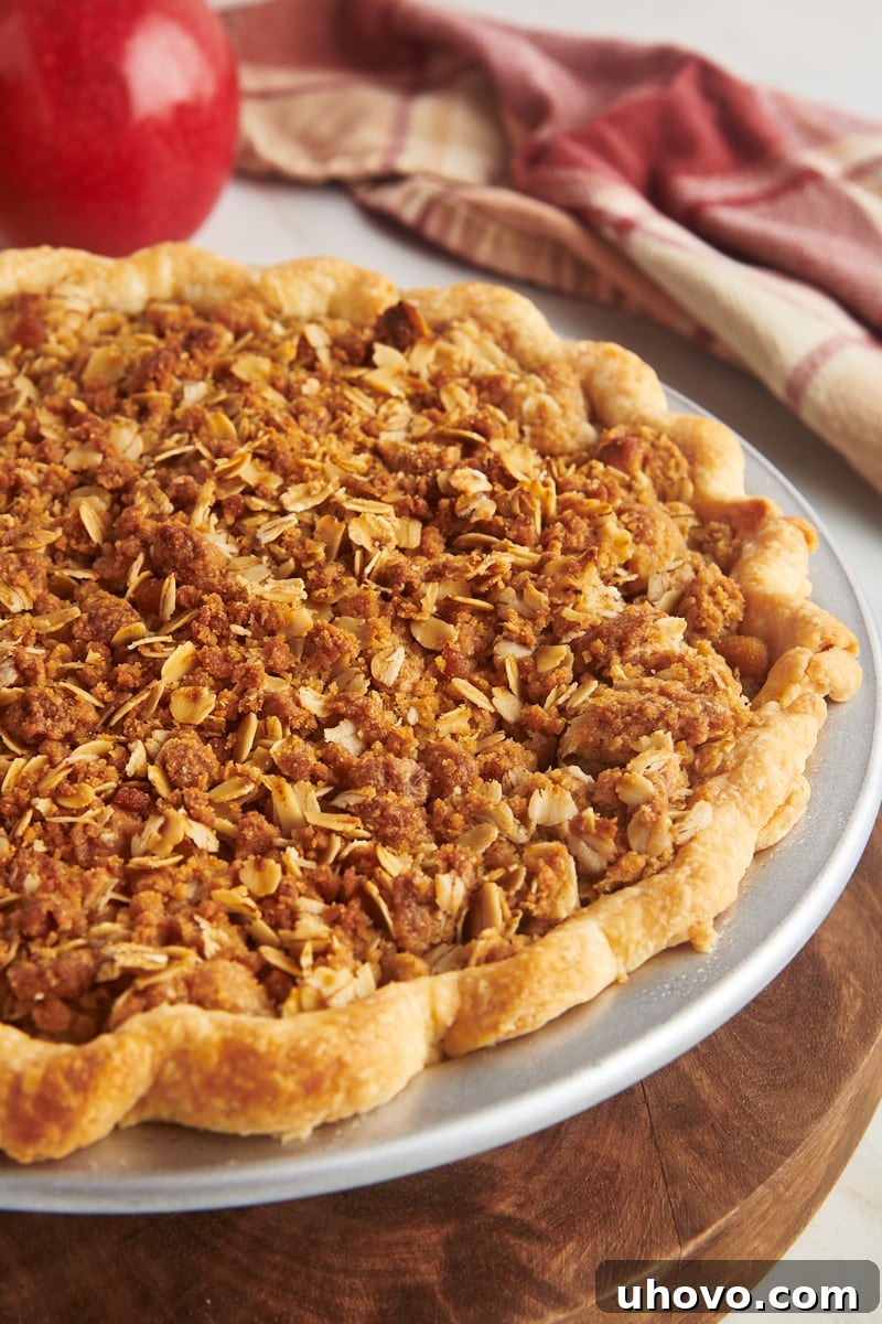 A freshly baked whole apple crumb pie, still in its metal pie pan, presented on a rustic wooden board, highlighting its appealing golden crust and textured crumble topping.