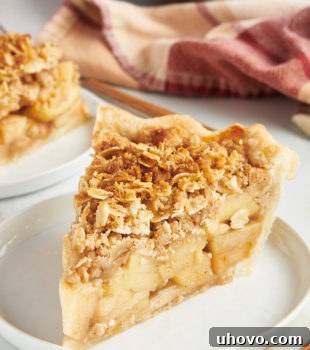 a slice of apple crumb pie on a white plate with more pie in the background