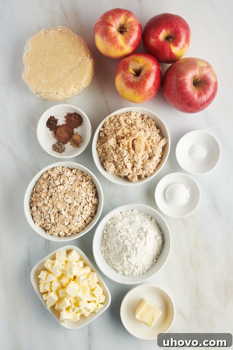 Overhead view of various fresh ingredients laid out on a clean white surface for making apple crumb pie, including sliced apples, flour, brown sugar, cinnamon, and oats.