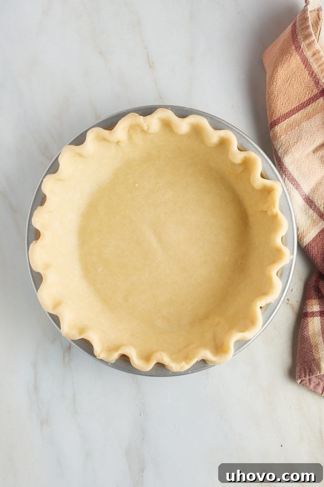 Overhead view of a perfectly rolled and crimped pie crust nestled in a 9-inch pie plate, ready for filling.