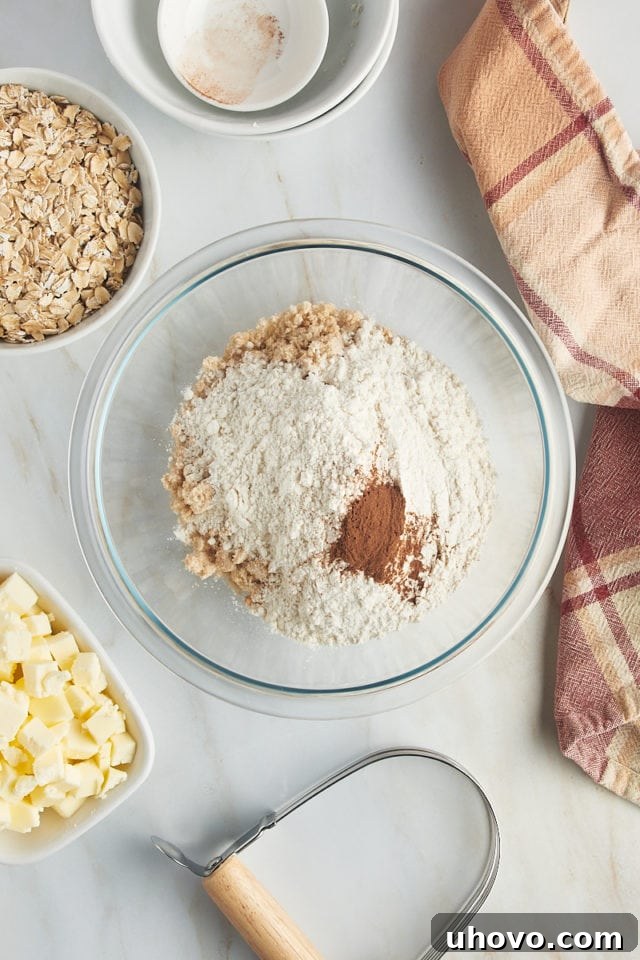 Close-up, overhead shot of dry ingredients – flour, brown sugar, cinnamon, and salt – meticulously measured into a clear glass mixing bowl, ready for the crumb topping.