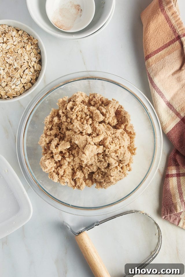 A glass mixing bowl with partially mixed crumb topping ingredients, showing the butter being cut into the dry flour mixture, forming small, rough crumbs.