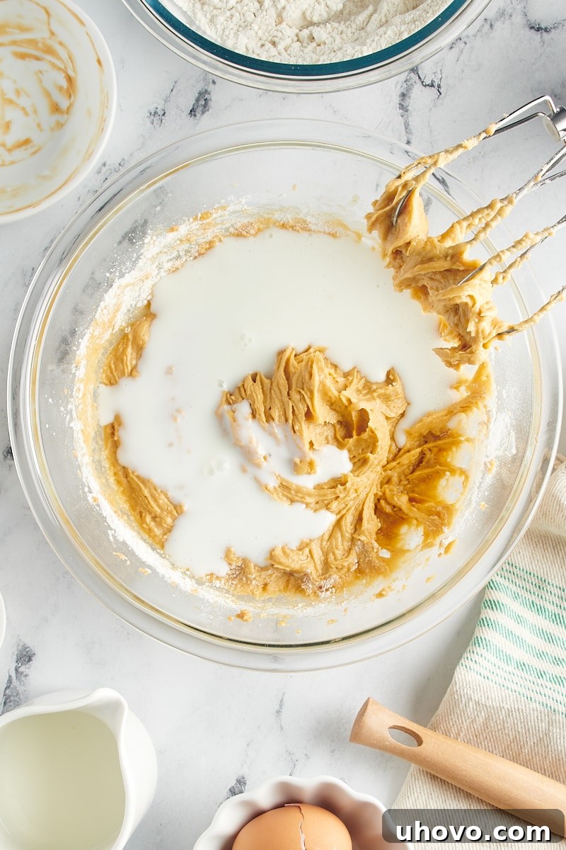 Overhead view of a portion of buttermilk being added to the batter in a mixing bowl, alternating with dry ingredients.