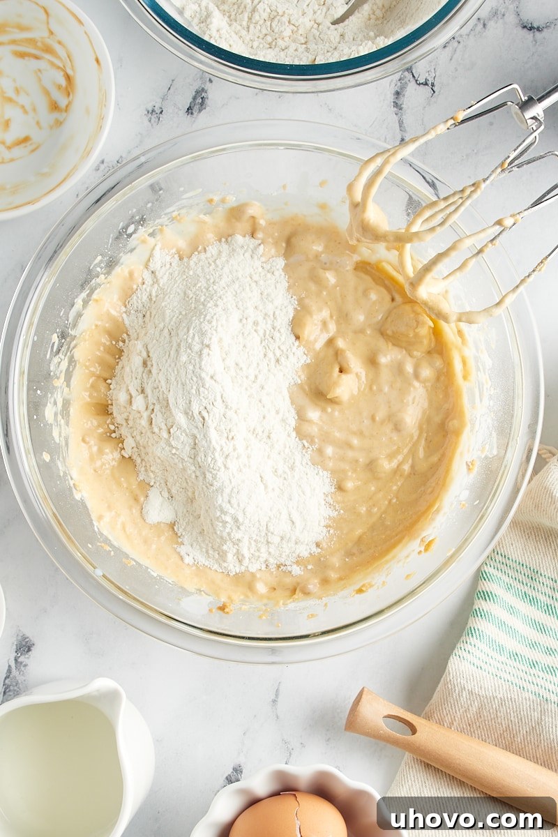 Overhead view of another portion of dry ingredients being added to the batter in a mixing bowl.